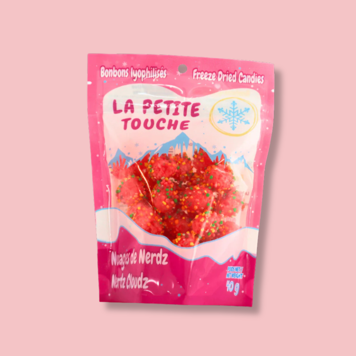 Sac de bonbons lyophilisés ‘Nuages de Nerdz’ de Confections La Petite Touche. L’emballage rose vif avec des montagnes enneigées évoque la légèreté et la douceur de ces bonbons croustillants. Une explosion de saveurs et de couleurs à chaque bouchée !