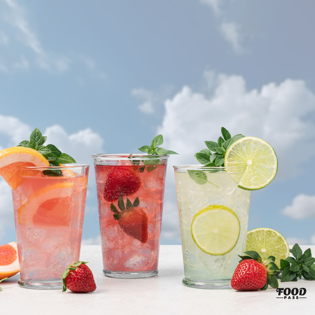 Trois verres de limonade pétillante aux agrumes, fraises et lime, garnis de menthe fraîche, sous un ciel bleu. Une boisson rafraîchissante et naturelle mettant en avant Flirt Drinks, produit vedette de la boîte FoodPass de février.